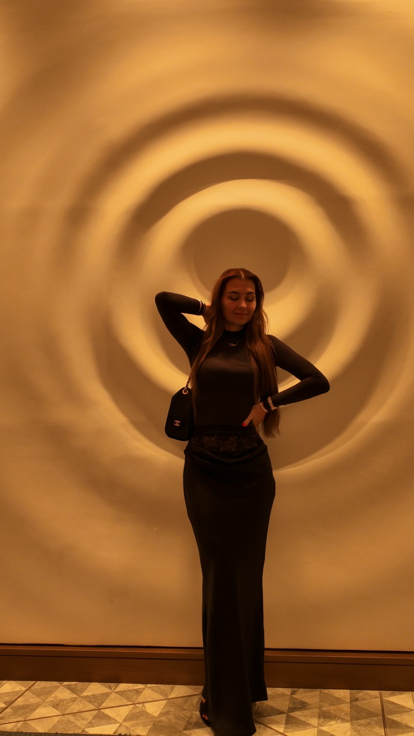 Dzanella, full length in one unbroken black column, still against a spiral wall.